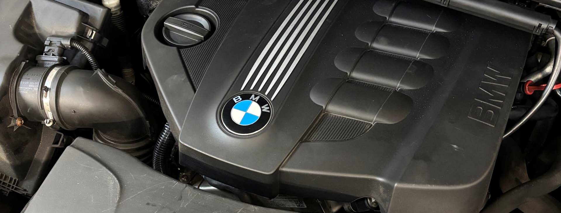 Ein BMW-Motor in einem Auto, schwarz mit silbernem BMW-Emblem und Abdeckung.