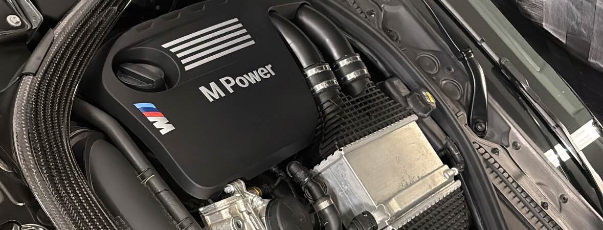 Ein graues Auto mit einem M Power Motor mit Kohlefaserteilen im Motorraum.